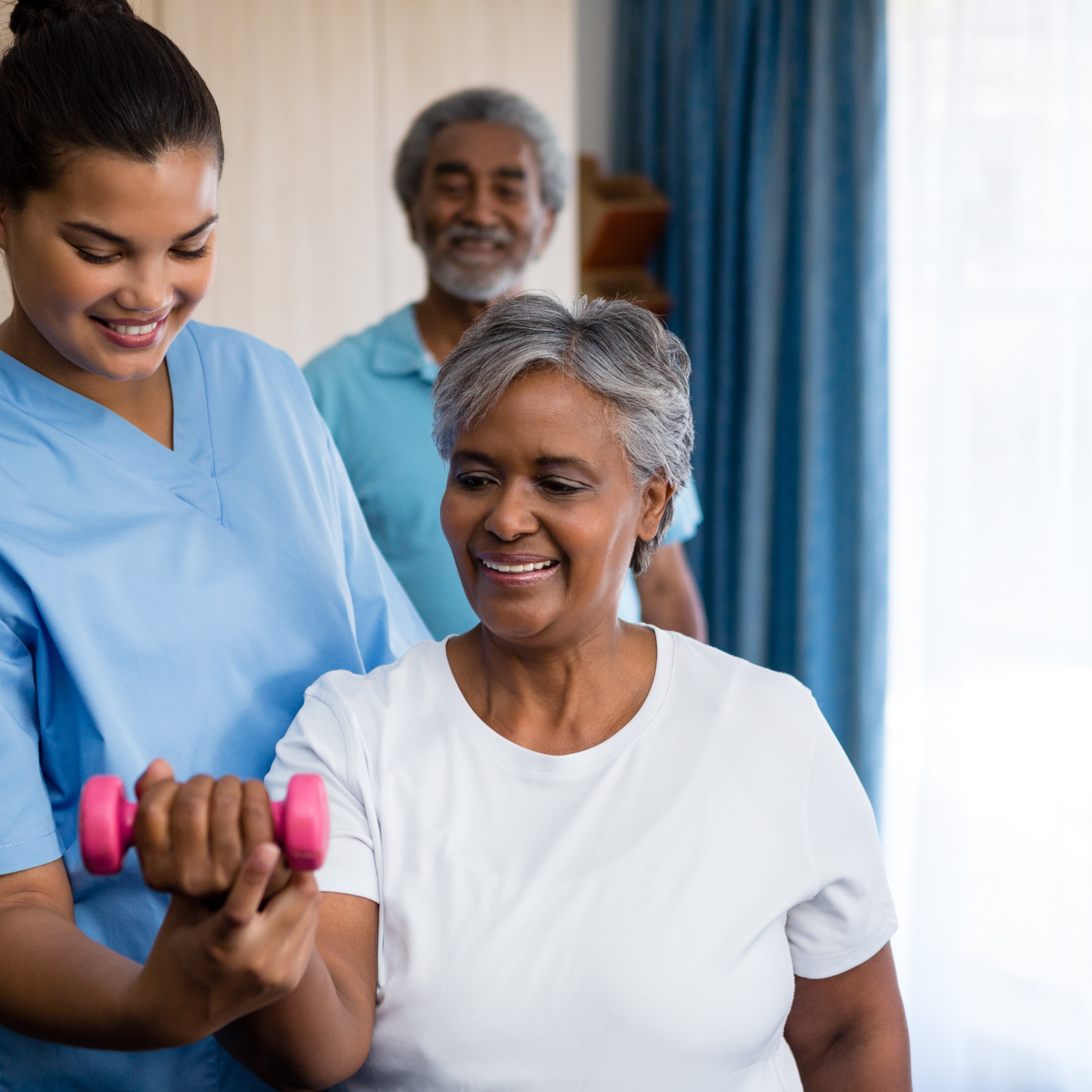 Nurse guiding senior woman in lifting dumbbell at retirement home